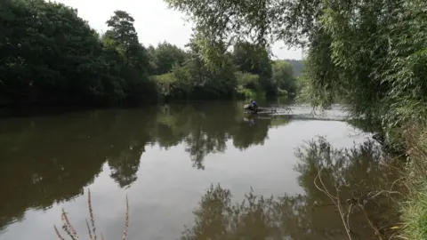 A photo of a river with banks and trees on either side of it