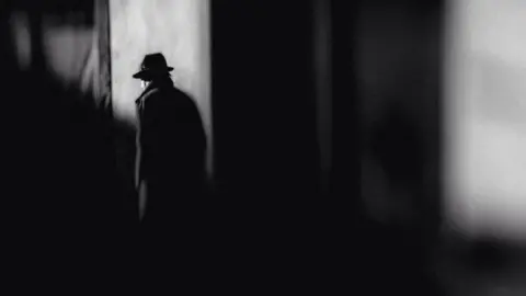 Getty Images Man in hat walking on street in shadow