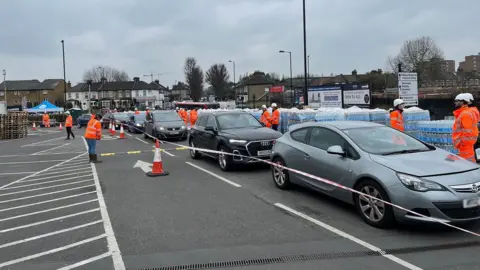 Cars queue at a water bottle station in Sainsburys car park