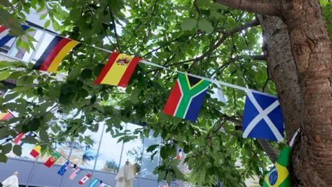 Flag bunting featuring flags from around the world, is tied to a tree.