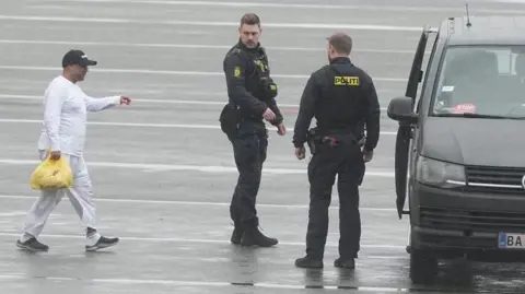 British businessman Sanjay Shah (left) is seen next to Danish police officers as he arrives at Kastrup Airport in Copenhagen in December 2023