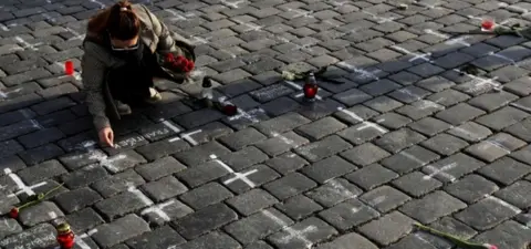 Reuters A woman writes a name next to a painted cross to commemorate Czech coronavirus deaths in Prague's Old Town Square
