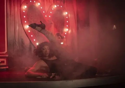 EPA Performers dressed in leotards and high heels flex their legs and pose on stage.