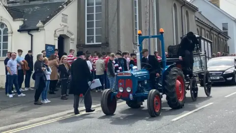 BBC a blue tractor carries the 16-year-old boy's coffin through the village