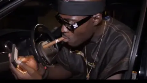 YouTube/Erikno Manolas Screen grab of French rapper Nick Conrad smoking a cigar, taken from his music video