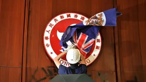 Getty Images - A protester attempts to cover the Hong Kong emblem with a British colonial flag after they broke into the government headquarters in Hong Kong on July 1, 2019