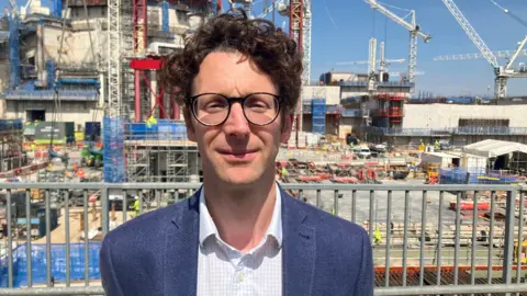 Andrew Cockcroft on site at Hinkley Point C staring into the camera with a half-smile and wearing glasses.