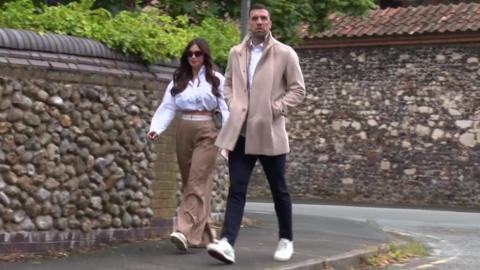 Shane Duffy in a beige coat, trousers and white trainers, arrives at court with a female who is wearing brown trousers, a white shirt and large sunglasses. 