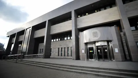PA Media An image of the front of the building at Glasgow Sheriff Court, an imposing grey modern structure with the Crown coat of arms above the revolving door, stern-looking marble pillars and three steps up to a paved area in front of the door.