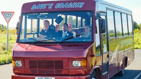 BBC/Toffee International Ltd/Tom Jackson Still from Gavin and Stacey showing actor Steffan Rhodri driving Dave's Coaches with Rob Brydon, James Corden, Larry Lamb and Alison Steadman as passengers.
