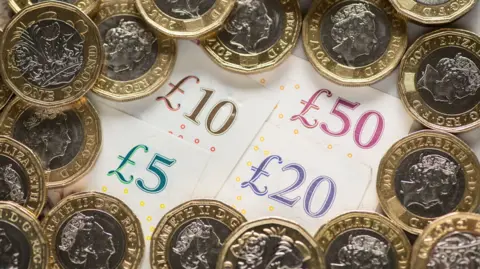 A picture of a UK five pound, ten pound, twenty pound and fifty pound notes surrounded by one pound coins. 