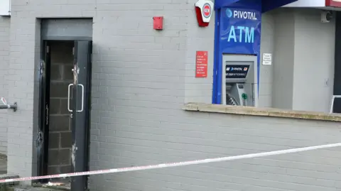 Pacemaker We see a building, with a door in the wall facing the camera - the door is black and lying open, with signs of damage. One the left hand side, on the other wall of the building, is an ATM