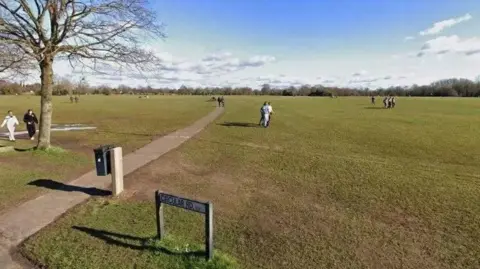 A wide green open space where people are strolling. A couple of trees are visible. A street sign reading "Circular Road" is visible in the foreground. 