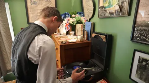 Jodie Halford/BBC Lincoln moves a gramophone needle on to a record in his bedroom. The bedroom wall is filled with black and white images.