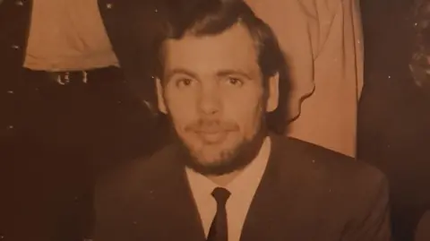 An old photo of Susan's father. It is a black and white pic of a beared man with dark hair in a smart dark suit with a thin white tie.
