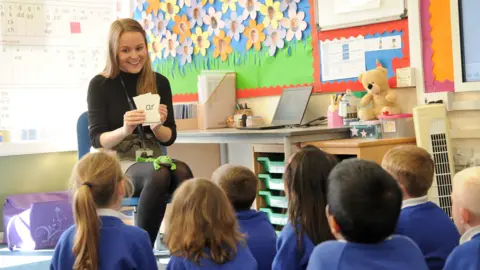 Oasis Community Learning Teacher Alice Cole teaching phonics to her class. She is sitting on her chair and the students are watching her teach the 'ar' sound