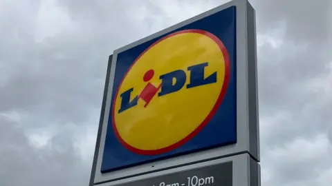 The Lidl sign, of blue and red letters against a yellow circle, under an overcast sky