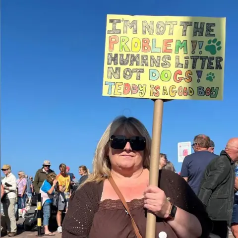 Protester Wendy Routledge wears brown and carries a sign 