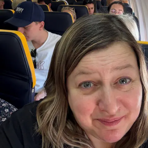 Emma Gale A selfie of Emma Gale sitting on a passenger plane. She has fair hair and grey eyes and is smiling at the camera.