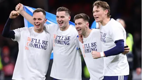 Getty Images Scotland's goal scorers (left to right) Lawrence Shankland, Kenny McLean, Kieran Tierney and Scott McTominay celebrate after the 4-2 victory over Denmark. They are wearing white commemorative t-shirts. They are waving a saltire. 