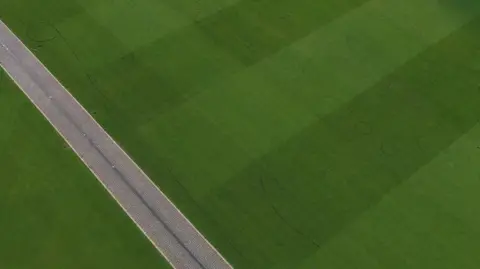 Dan Jessup An aerial view of a tennis court. There are deep lines running across the lawn.