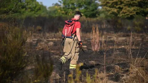 A firefighter in a red T-shirt cools down an area of ground after a fire was extinguished.