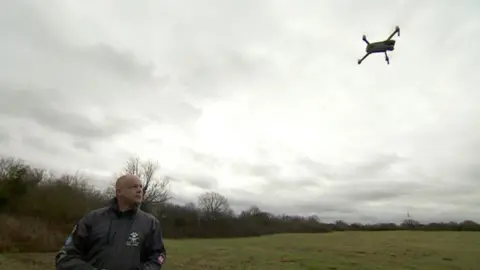 Phil James standing in a field while flying a drone