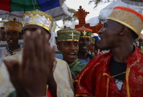 Andalou via Getty Images An Ethiopia priest wearing a green traditional cap has his mouth open as he chants.