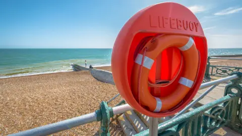 Getty Images A bright orange life ring behind a railing next to a beach