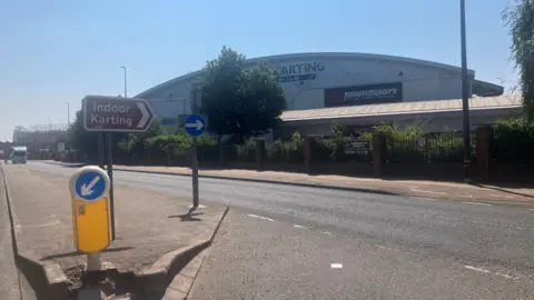 Photograph of an indoor go-karting track in Trafford Park. The image shows a road, with a traffic sign and a warehouse in the background.