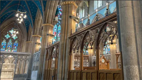 Ornate, lit cathedral with blue starred ceiling and wooden carved structures.