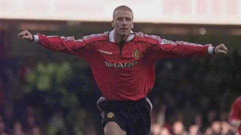 David Beckham, in a red Man Utd shirt, wheels away with his arms outstretched after scoring a free-kick against Leicester City