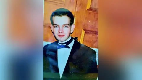 Bobby Bradley Robert Bradley wearing a black bow tie and black suit with a white shirt. He has short brown hair. 