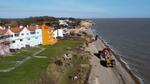 Jamie Niblock/BBC A drone image of the Thorpeness coastline. A large piece of machinery delivering rock bags can be seen on the beach.