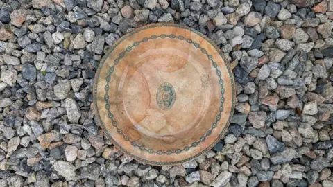 Dominic Robinson A picture of the crockery which is green and brown in colour. It is pictured in the middle of a number of stones on the floor.