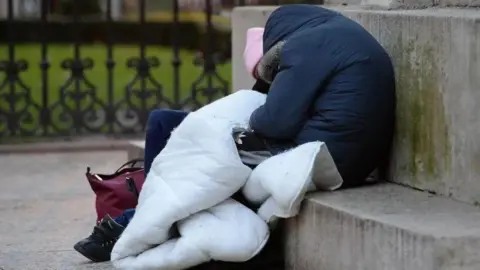 Two homeless people sit slumped on a concrete step outside.