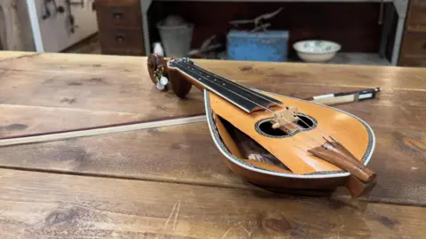PA Media  A small, yellow lyra and its bow, resting on a wooden table.
