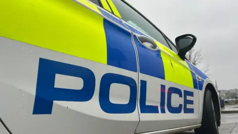 A police logo on the side of a police car. The vehicle has blue and yellow stickers on its exterior.