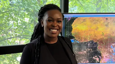 Sarah Kimani Sarah Kimani of the Kenya Meteorological Department stands in front of a weather map.