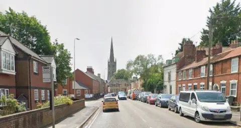 Google A picture looking down the road towards a church. Terraced properties are on both sides of the road.