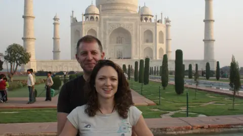 Jo O'Connell Jo O'Connell is pictured with her husband at the Taj Mahal. He stands behind with his arms around her waist. She has curly, brown hair over her shoulders and a light T-shirt. He has receding brown-grey hair and dark T-shirt.