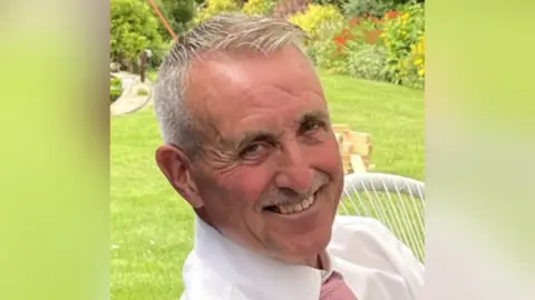 North Yorkshire Police An older man with short grey hair, sitting in a garden, smiles at the camera.