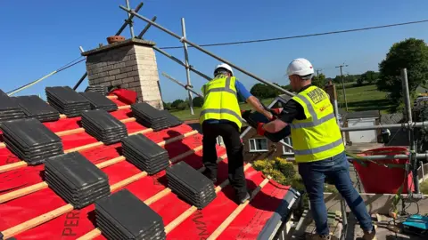 Band of Builders Workmen in hi-vis jackets and white helmets carry out repairs to a roof.