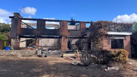 The shell of a two-storey fire-damaged home with its roof and windows missing