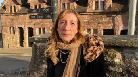 A woman with red hair wearing a black coat with gold scarf