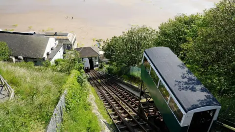 A view looking down Scarborough's Spa Cliff Lift. Railway tracks run vertically down a steep cliff with a building at the bottom of the track. An expanse of sandy beach can be seen below.