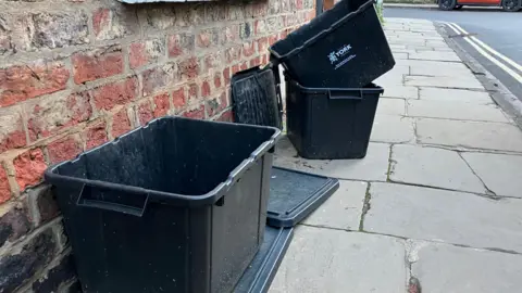 A couple of black boxes with lids outside a terraced house in York