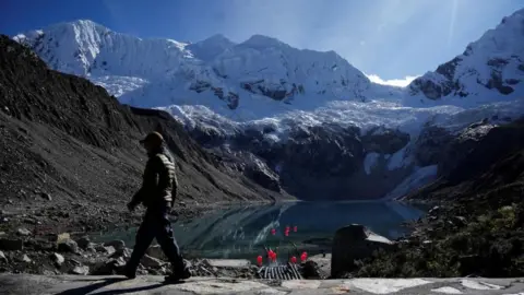 Reuters Mr Lliuya is seen walking in front of Palcacocha Lake, in the Peruvian Andes. Snow-capped glaciers can be seen in the background.