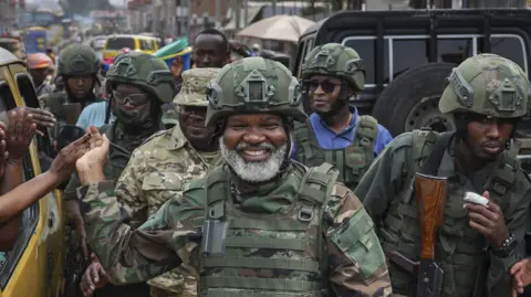 Corneille Nangaa, wearing military fatigues and a helmet and surrounded by rebel fighters, shakes hands with passengers in a public service taxi in the city of Goma on February 1, 2025. 