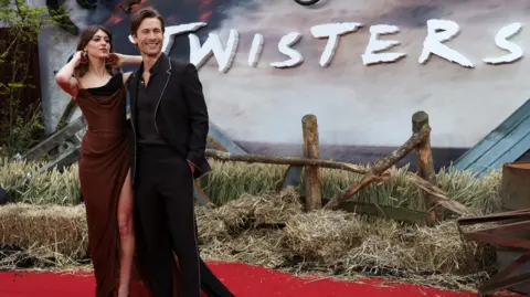 EPA Daisy Edgar-Jones and Glen Powell on a red carpet in front of a large sign saying Twisters